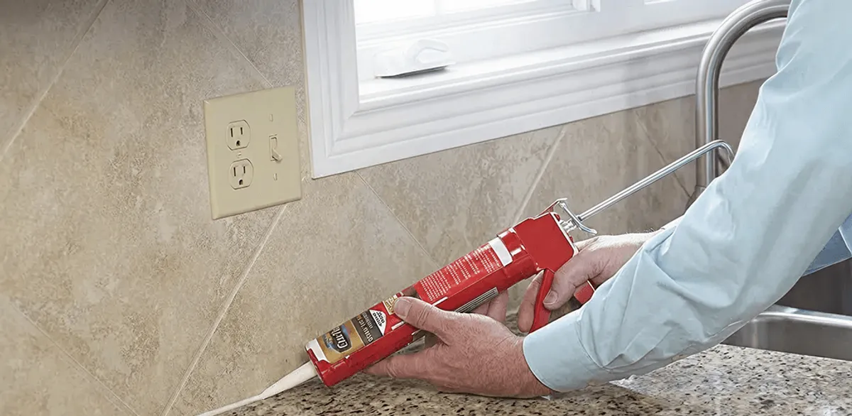 Handyman applying caulk along a kitchen backsplash and countertop seam in Lakewood, CO
